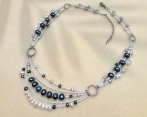 Multi strand necklace with vintage pearls, seed beads, and metal components lying on a cream-colored fuzzy mat with a blurred light shadows of leaves over it