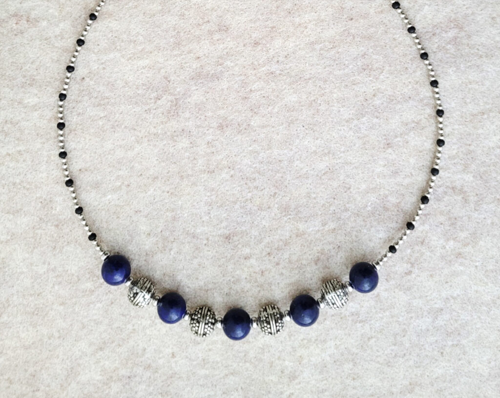 single string necklace with round dark blue lapis lapis, black seed beads, and various white metal beads